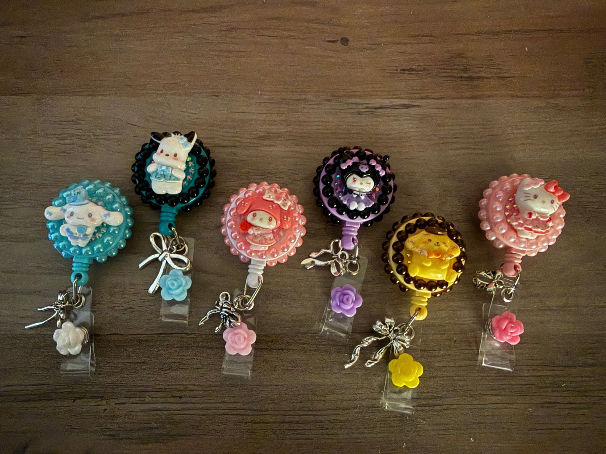 Six handcrafted Sanrio-themed retractable badge reels with pearls and charms on a wooden surface.