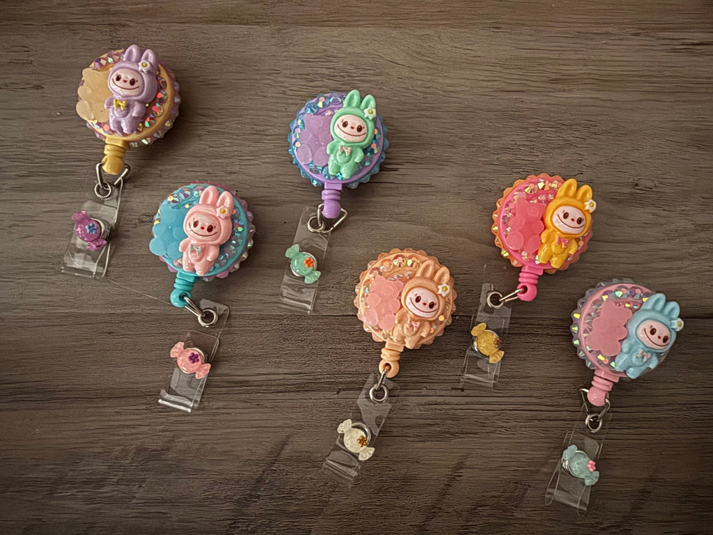 Six handmade retractable badge reels embellished with colorful rhinestones and pastel monster charms in bunny suits.