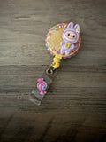 Handmade purple monster badge reel embellished with pink rhinestones, a yellow gummy bear, and a purple candy charm.