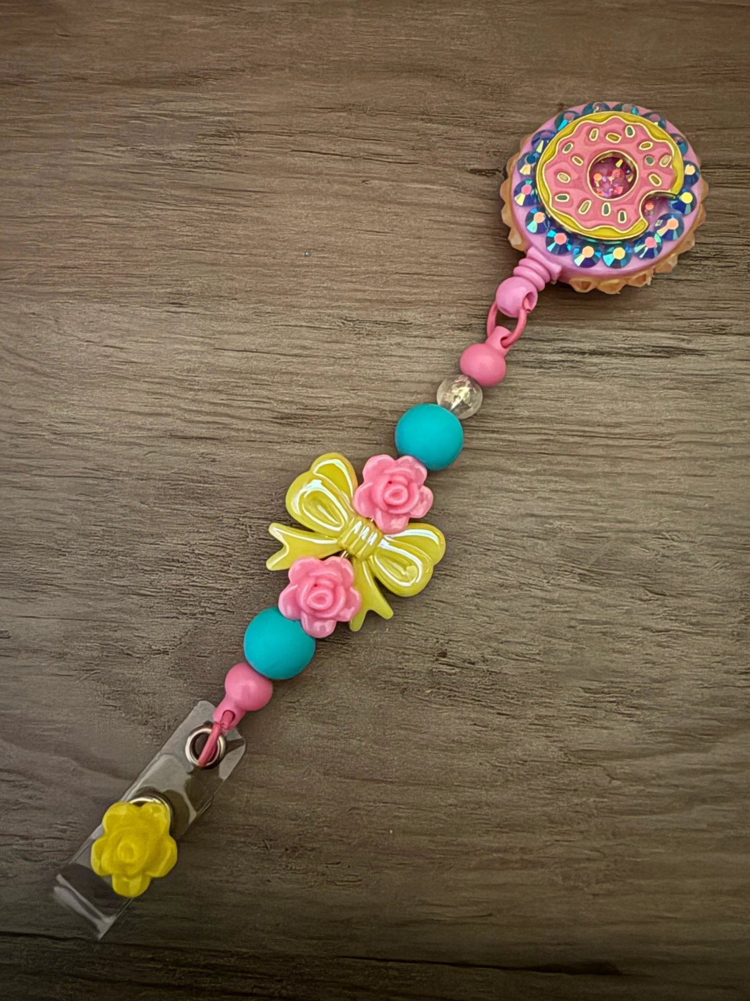 Colorful badge reel featuring a donut design, embellished with pink and turquoise beads, flower accents, and a yellow bow.