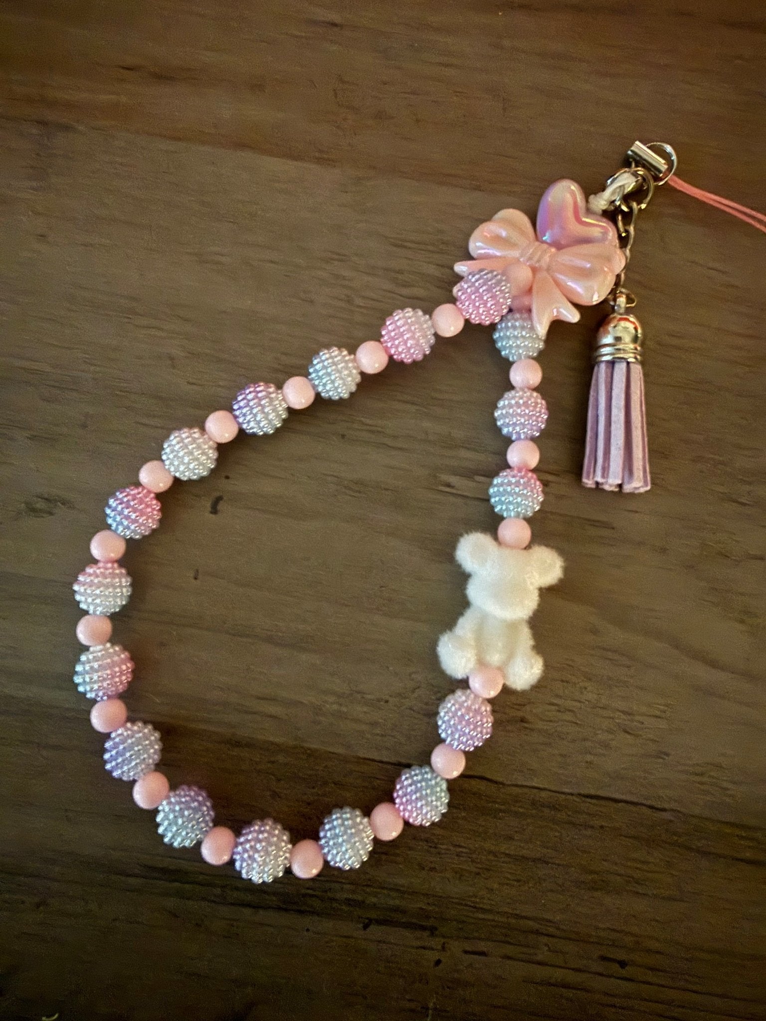 Handmade light pink and white beaded phone wristlet with a fuzzy white teddy bear, a pink bow, and a matching tassel.