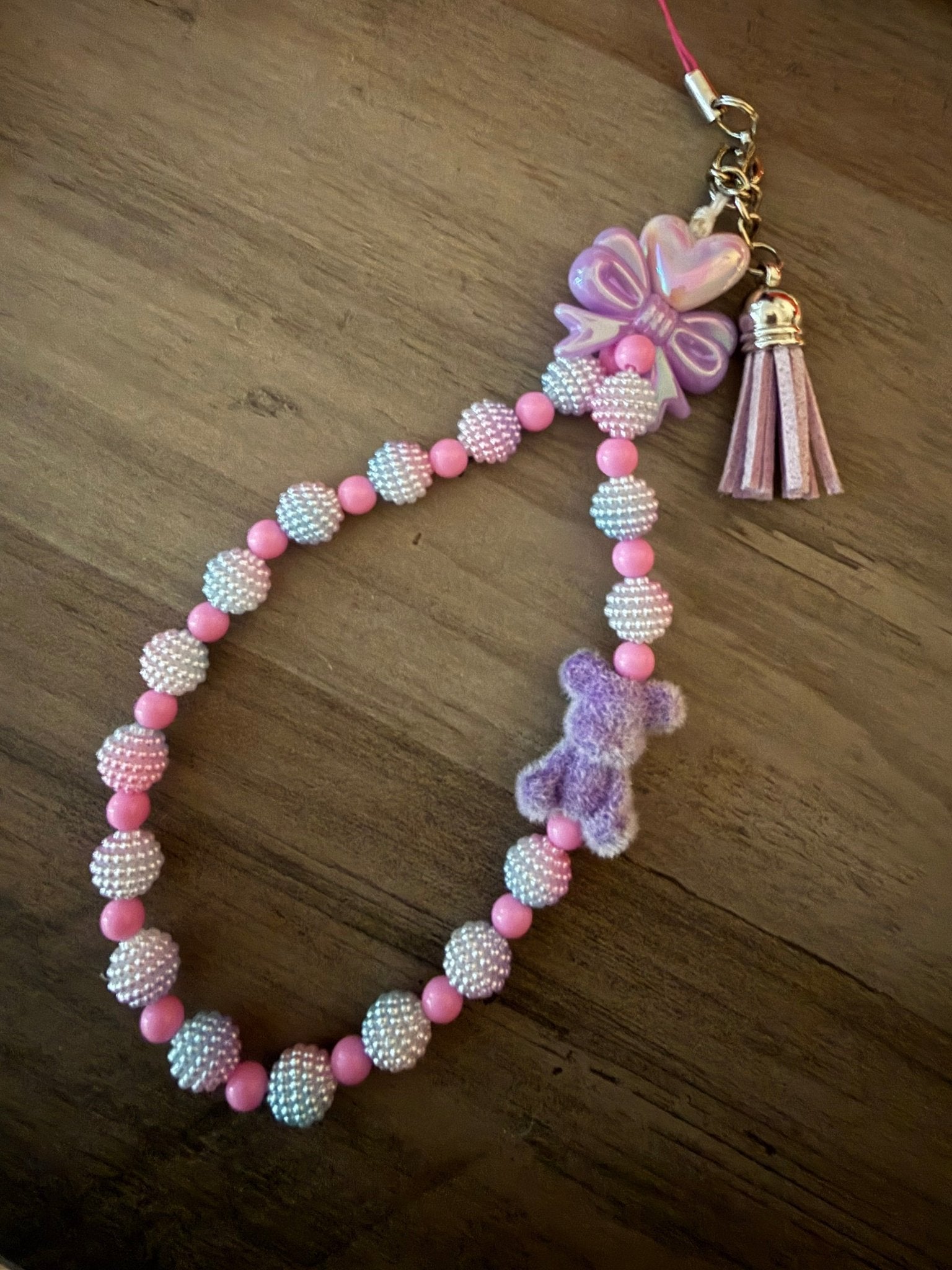Handmade purple and pink beaded phone wristlet with a fuzzy purple teddy bear, a lavender bow, and a matching tassel.
