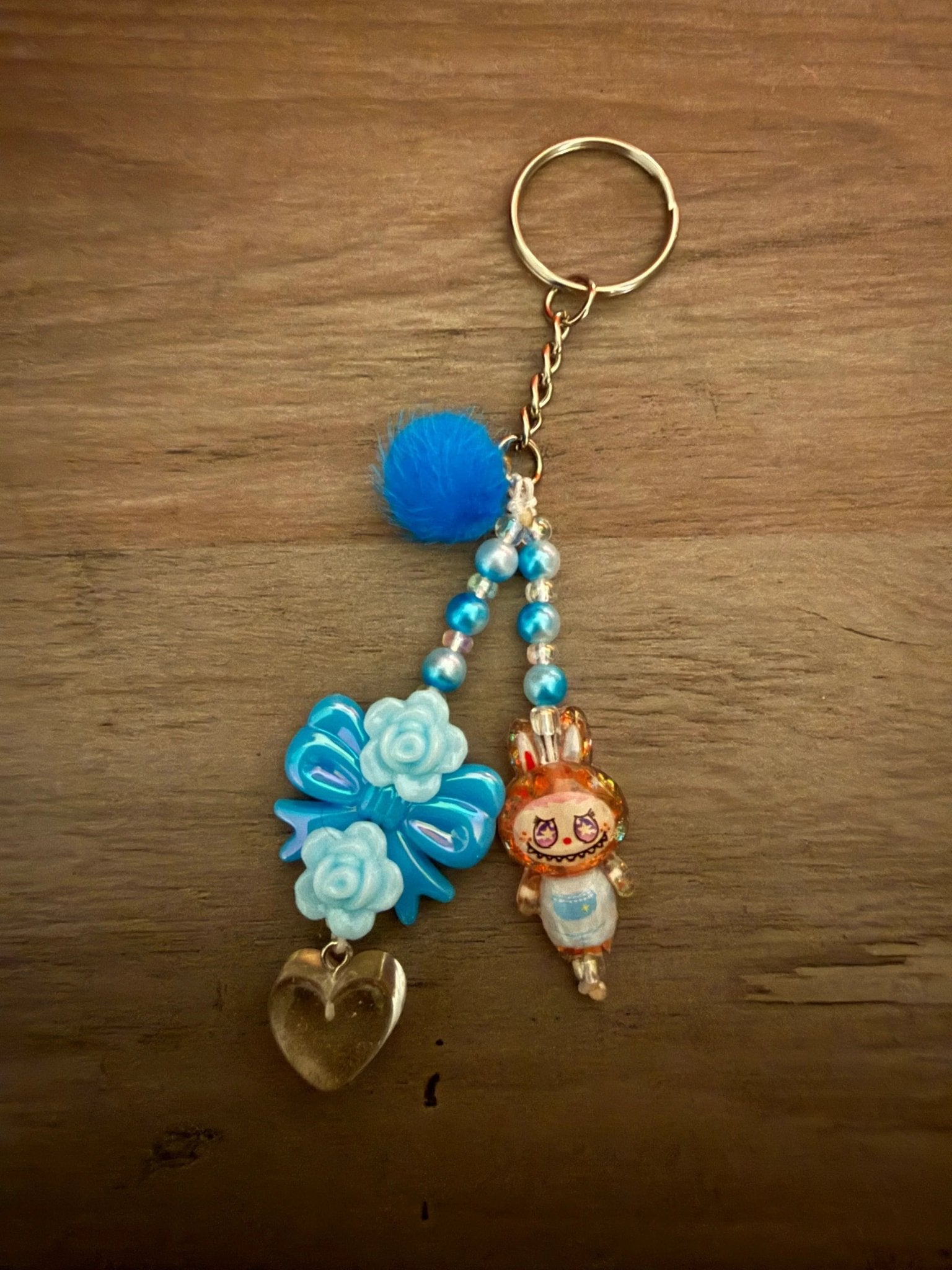 Colorful keychain with a blue fluffy pom-pom, a blue bow, a heart charm, and a cute character figure, and vibrant beads.